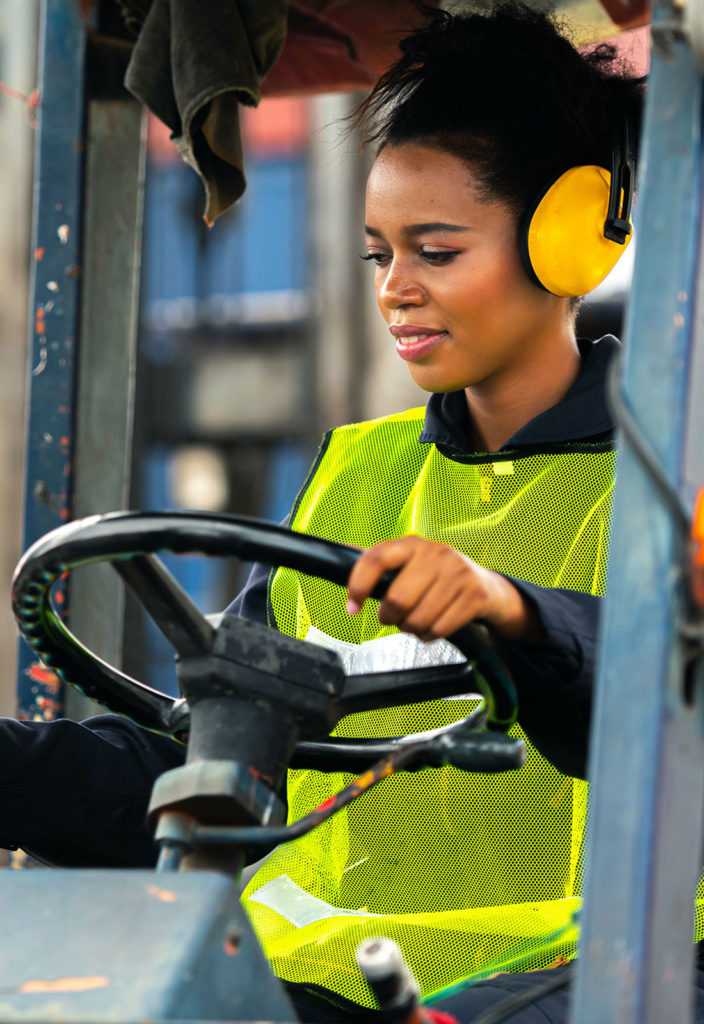 Female worker driving forklift in industrial container warehouse